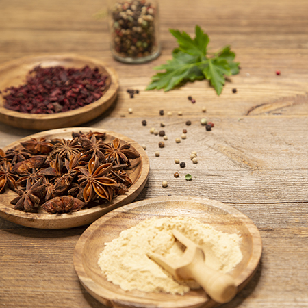 Star anise, red parts of the plant and colored pepper lie in bowls on a wooden table