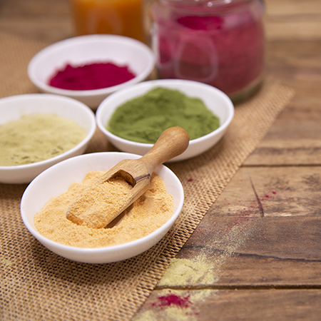 Four white bowls with colorful plant powder are on a wooden table