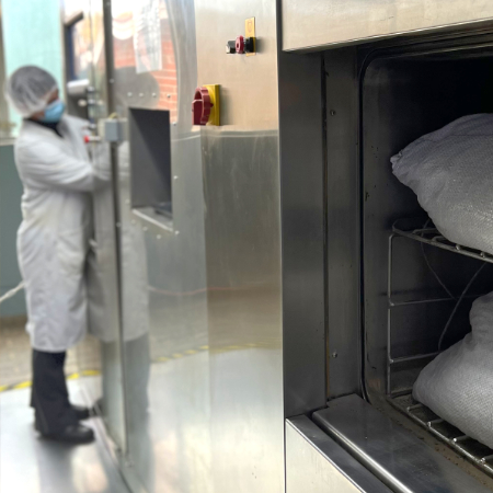 a person in a white protective suit operates a large machine to protect stocks of plant-based raw materials