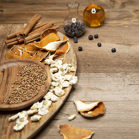 Ingredients like cinnamon sticks, orange peel, juniper berries, seeds and flowers are decorated on a wooden bowl